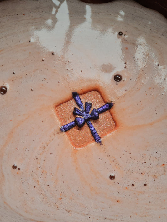 Foaming bath bomb in a christmas present design in orange and purple