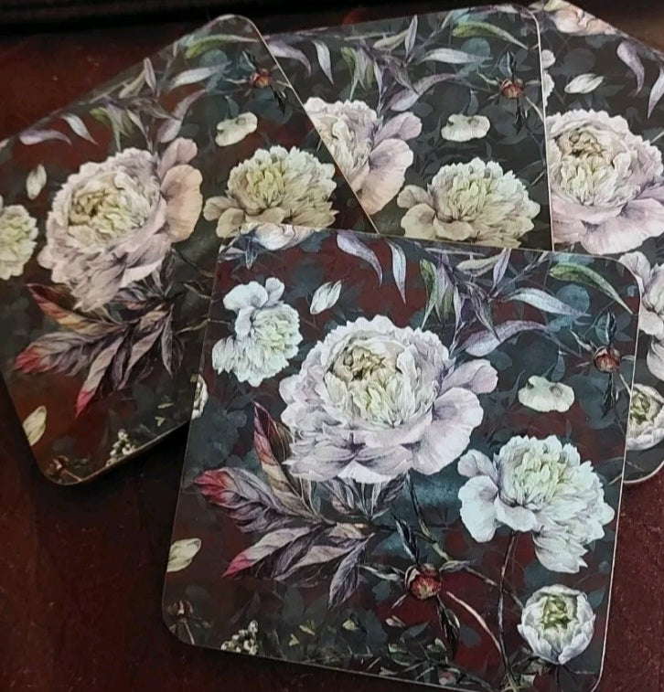 Set of floral coasters with white flowers and green leaves on a dark background.