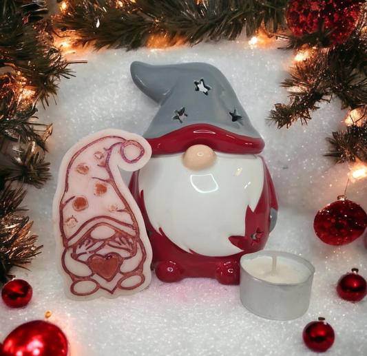 A ceramic gonk wax and oil warmer with a grey hat and a pink button nose, displayed with a scented wax melt and a tea light candle, against a Christmas-themed backdrop.