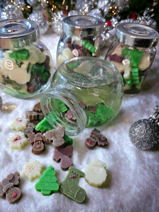 Jars with Christmas-shaped wax melts, scattered around with a few decorative holiday ornaments, with a focus on the wax melts which are green, white, and brown, representing a festive appearance.